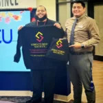 Owner of Structured Society LLC, Xavier Velez, smiling and holding up branded company apparel alongside an AmeriCU representative inside the AmeriCU Credit Union branch.